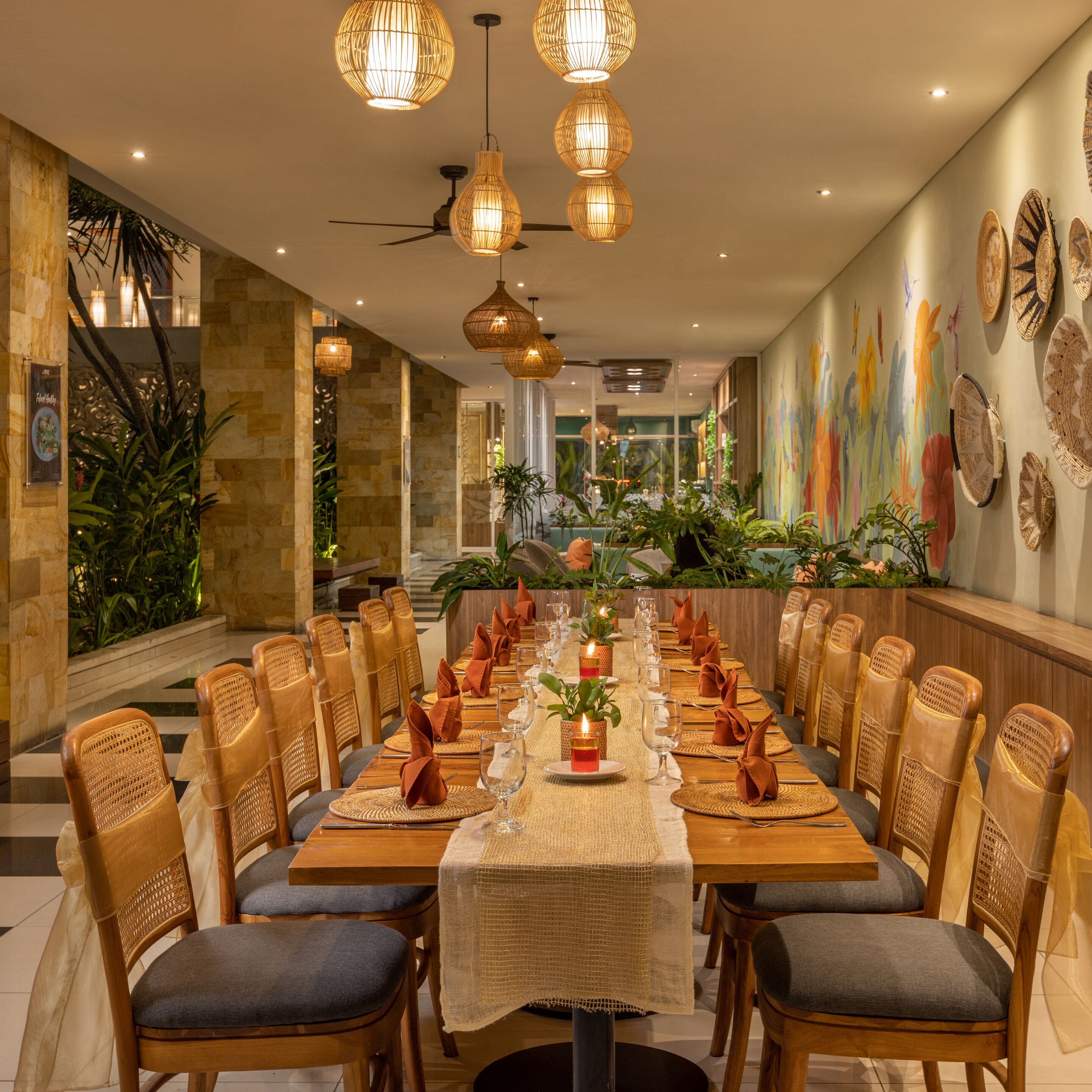 A long dining table with chairs, overhead lighting, and a mural on the wall.