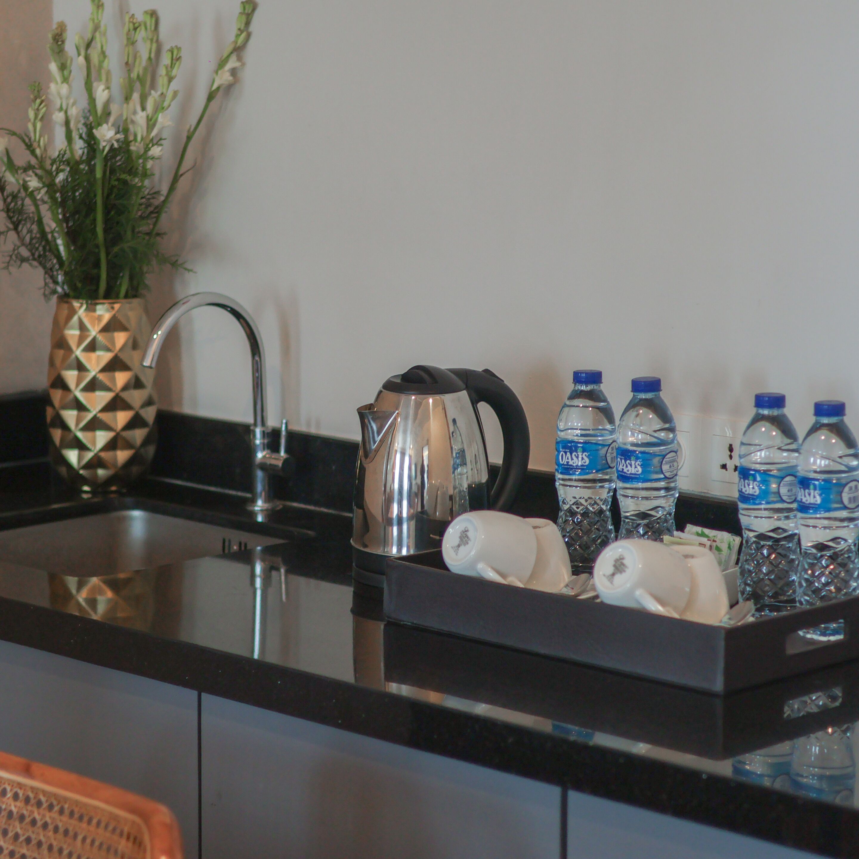 A kitchen with a sink, a kettle, a vase with flowers, and several water bottles.