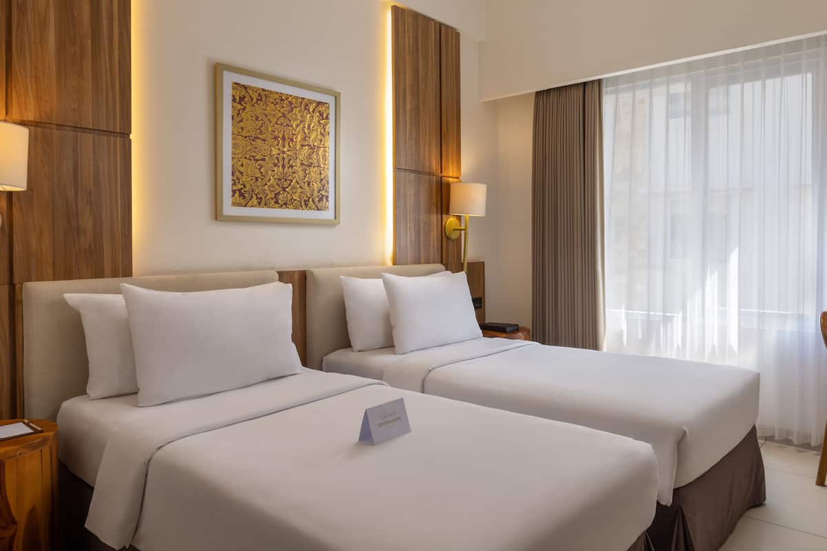 A hotel room with two beds, a framed artwork on the wall, and a window with curtains.