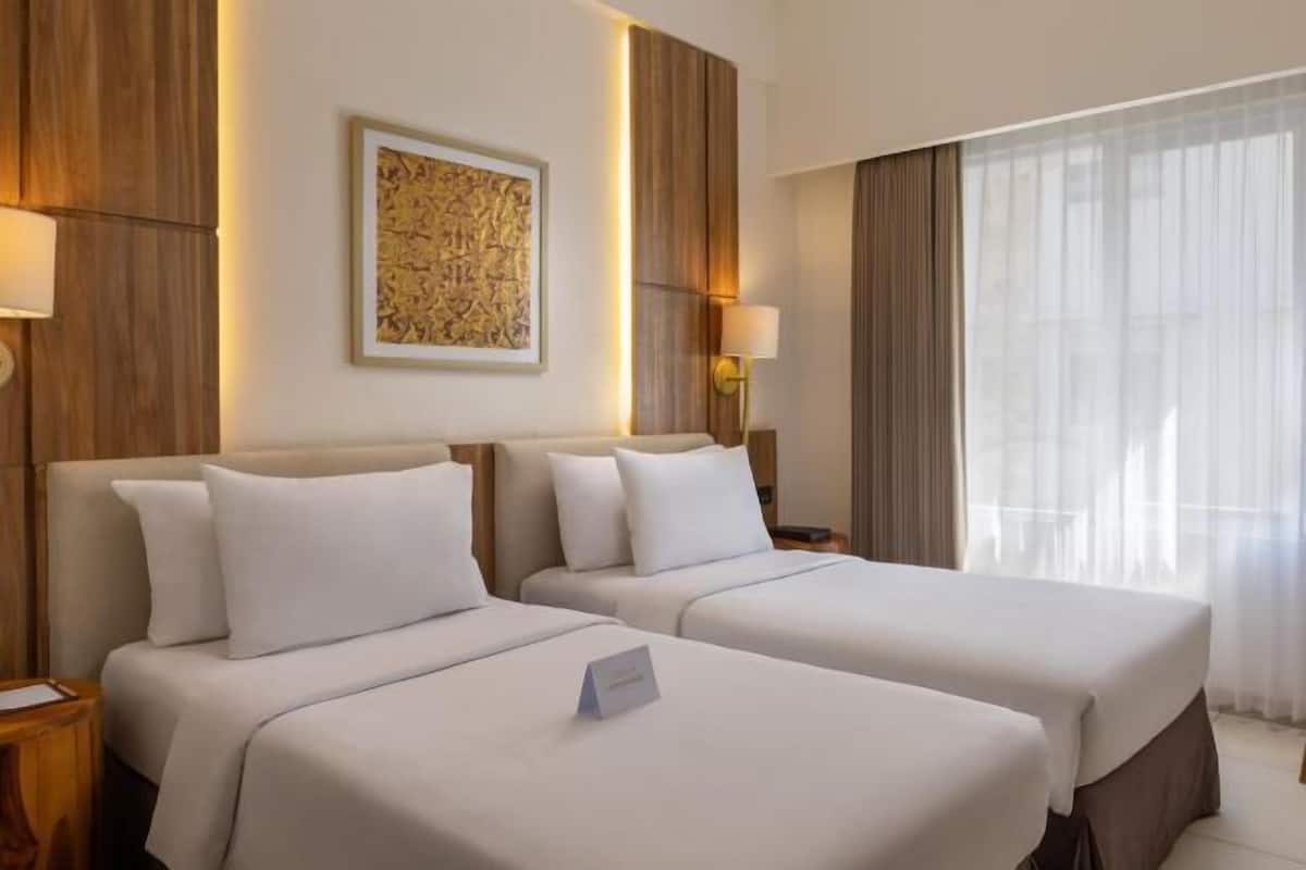 A hotel room with two beds, a framed artwork on the wall, and a window with curtains.