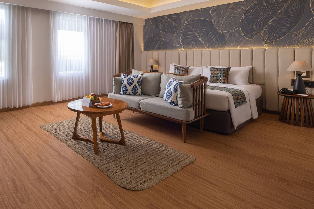 A modern hotel room with a sofa, a bed, a round table, and a large abstract wall art piece.
