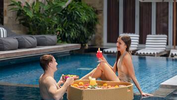 A couple relaxing by a poolside with a wicker basket of food and drinks.