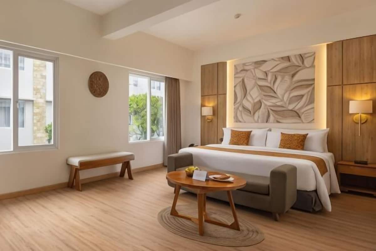 A hotel room with a large bed, a bench, a round table, and a wall with a leaf pattern.