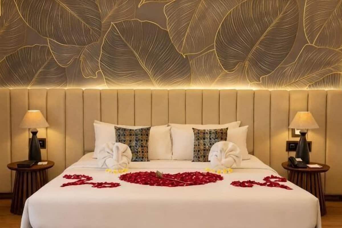 A hotel room with a large bed, two bedside tables, a wall with a leaf pattern, and a headboard.