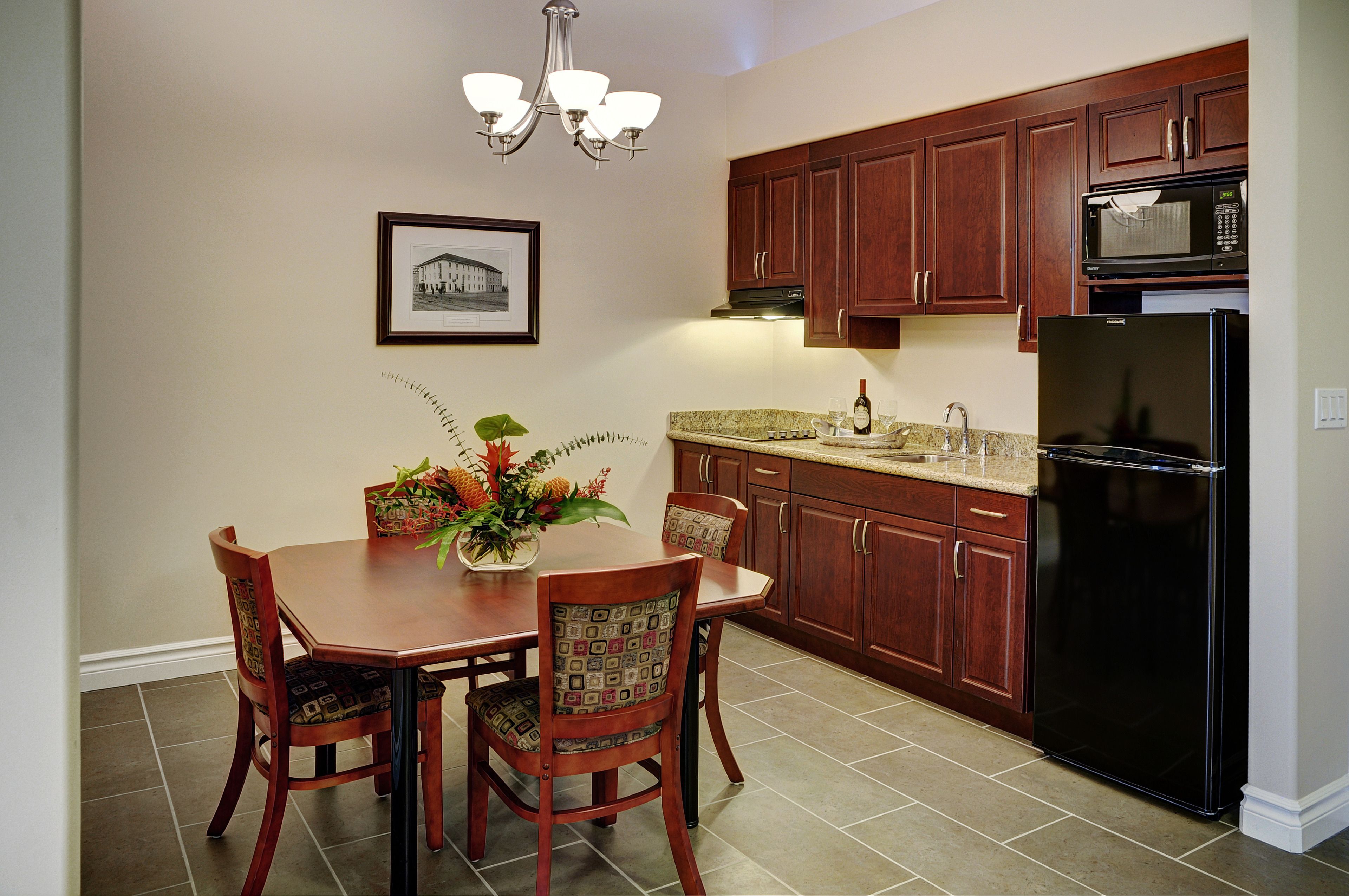 A kitchen with wooden cabinets, a black refrigerator, a microwave, and a dining table with chairs.