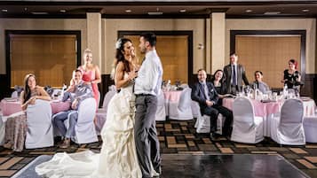 A wedding reception with guests seated at round tables, a dance floor, and a stage area.