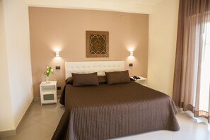 A bedroom with a large bed, two bedside tables, a nightstand, a wall-mounted lamp, and a decorative wall piece. - 4 Spa Hotel (Aci Castello)