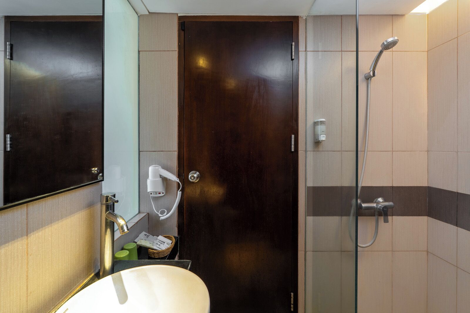 Un baño con una puerta de madera oscura, una ducha con cabezal de ducha manual, un espejo y un lavabo con toallero.