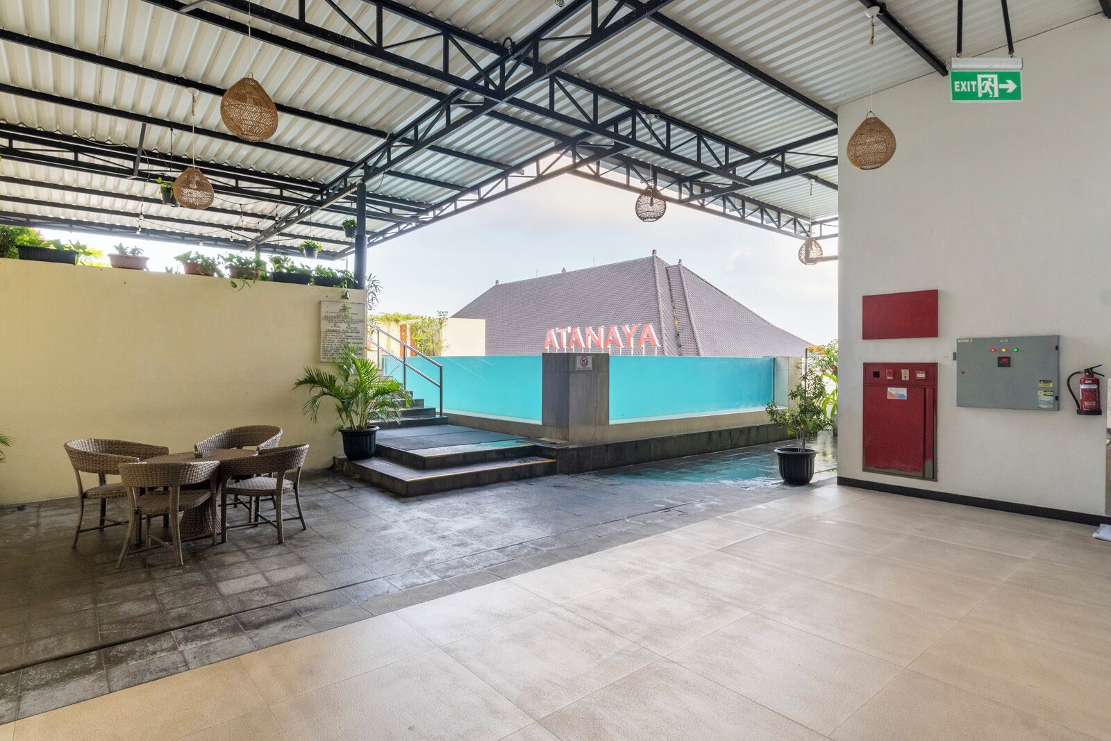 Un espacio al aire libre techado con una mesa, sillas, una escalera y un edificio con la señalización 'ATANAYA'.