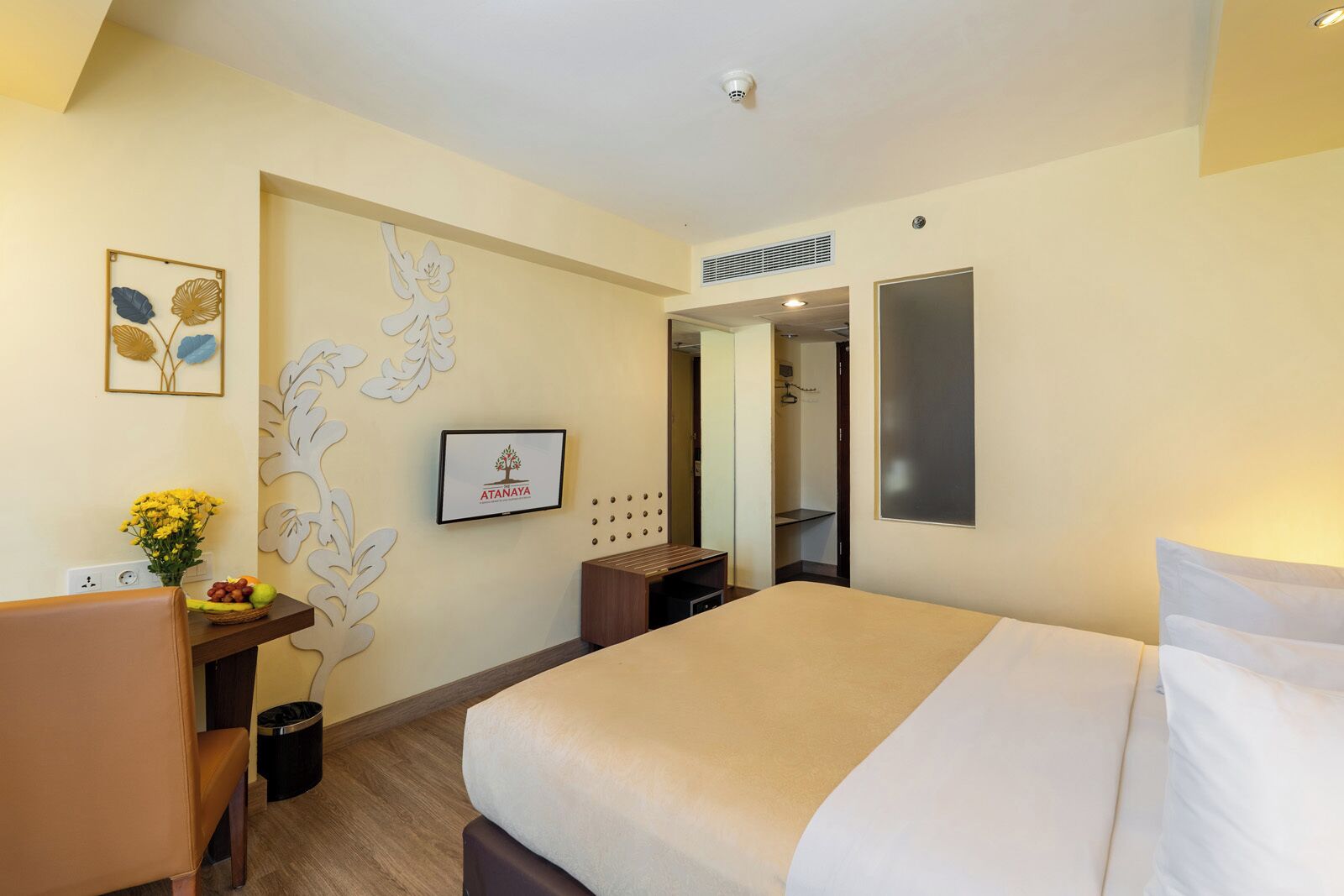 A hotel room with a bed, desk, chair, and a wall-mounted mirror.