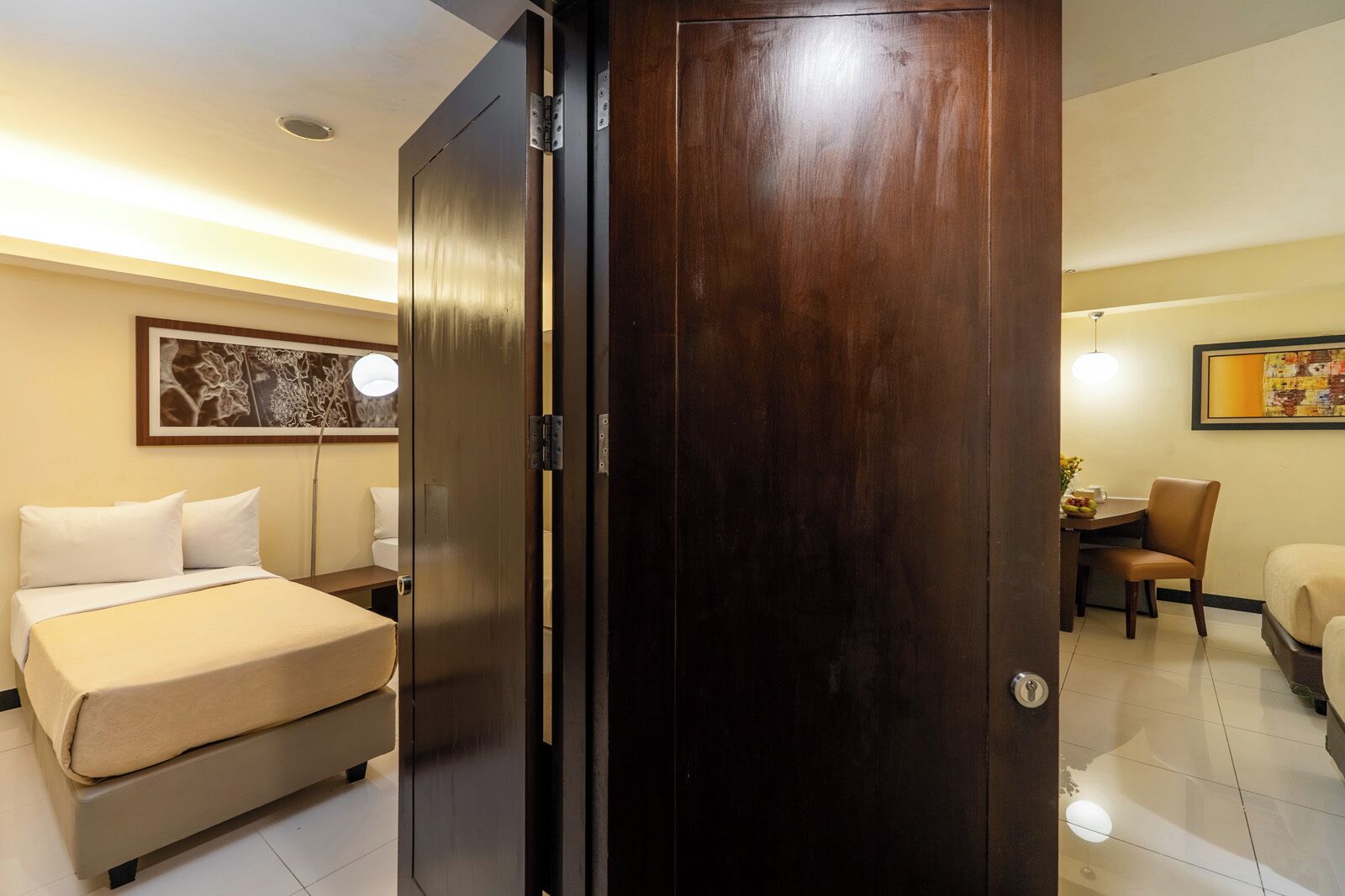 A hotel room with a bed, a desk, a chair, a wooden wardrobe, and a painting on the wall.