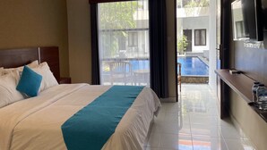 A hotel room with a bed, a TV, and a view of a swimming pool. - Seminyak Point Guest House (Seminyak)