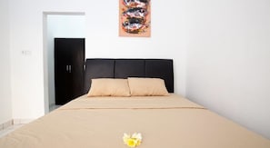 A bedroom with a bed, a dark headboard, a beige bedspread, and a painting of fish on the wall.