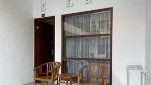A room with two wooden chairs and a small table, a large window with curtains, and a door with a number sign. - Seminyak Point Guest House (Seminyak)