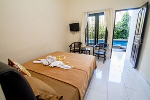 Habitación de hotel con cama, televisor, balcón con sillas y vista a la piscina.