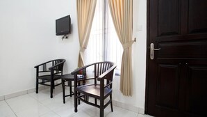 A room with two wooden chairs, a small table, a mounted TV, and a dark wooden door. - Seminyak Point Guest House (Seminyak)