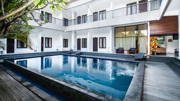 A multi-level building with a central swimming pool, balconies, and a reception area with a flower arrangement. - Seminyak Point Guest House (Seminyak)