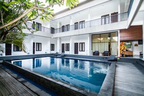 A multi-level building with a central swimming pool, balconies, and a reception area with a flower arrangement. - Seminyak Point Guest House (Seminyak)