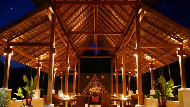 An outdoor dining area with tables and chairs under a wooden pavilion with a starry night sky in the background.