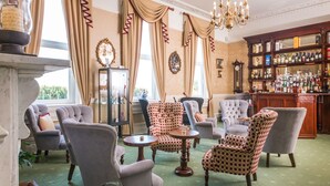 A room with multiple armchairs, a round table, a bar area with shelves of bottles, and a large mirror on the wall.