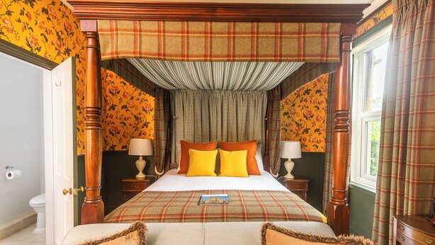 A four-poster bed with a plaid bedspread, two nightstands with lamps, and floral wallpaper. - Oldfields House (Bath)