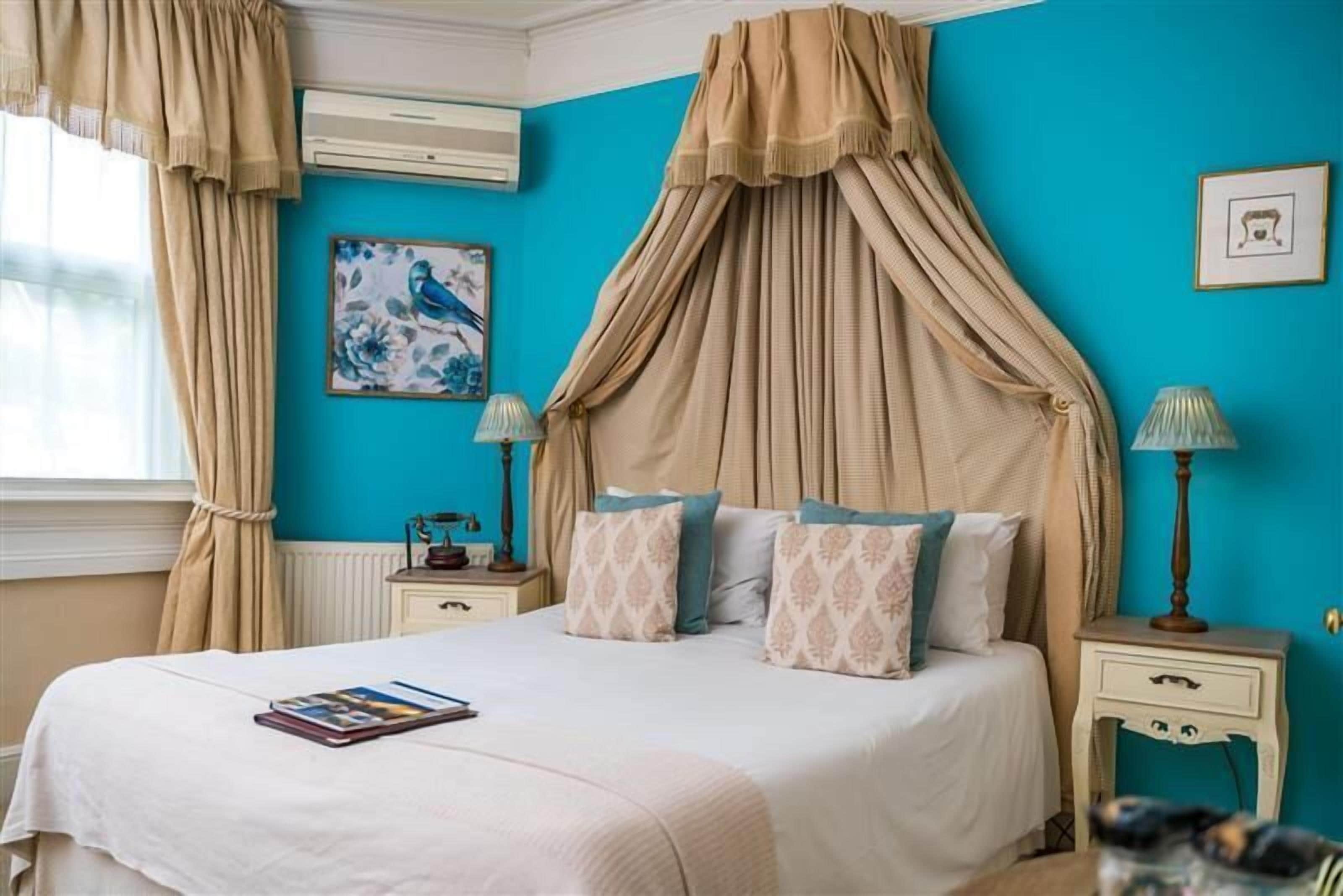 A bedroom with a canopy bed, a blue accent wall, and a framed artwork.