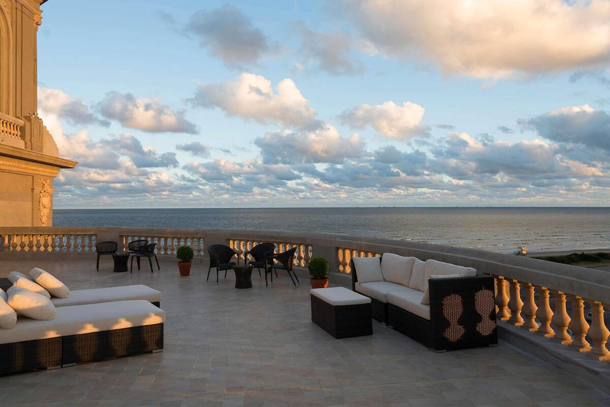 Een terras met zitplaatsen buiten, uitzicht op de zee en een gevel.