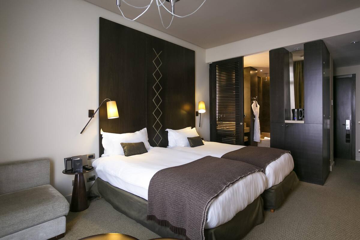 Une chambre d’hôtel moderne dotée d’un grand lit, de deux tables de chevet, d’un coin salon et d’un dressing.