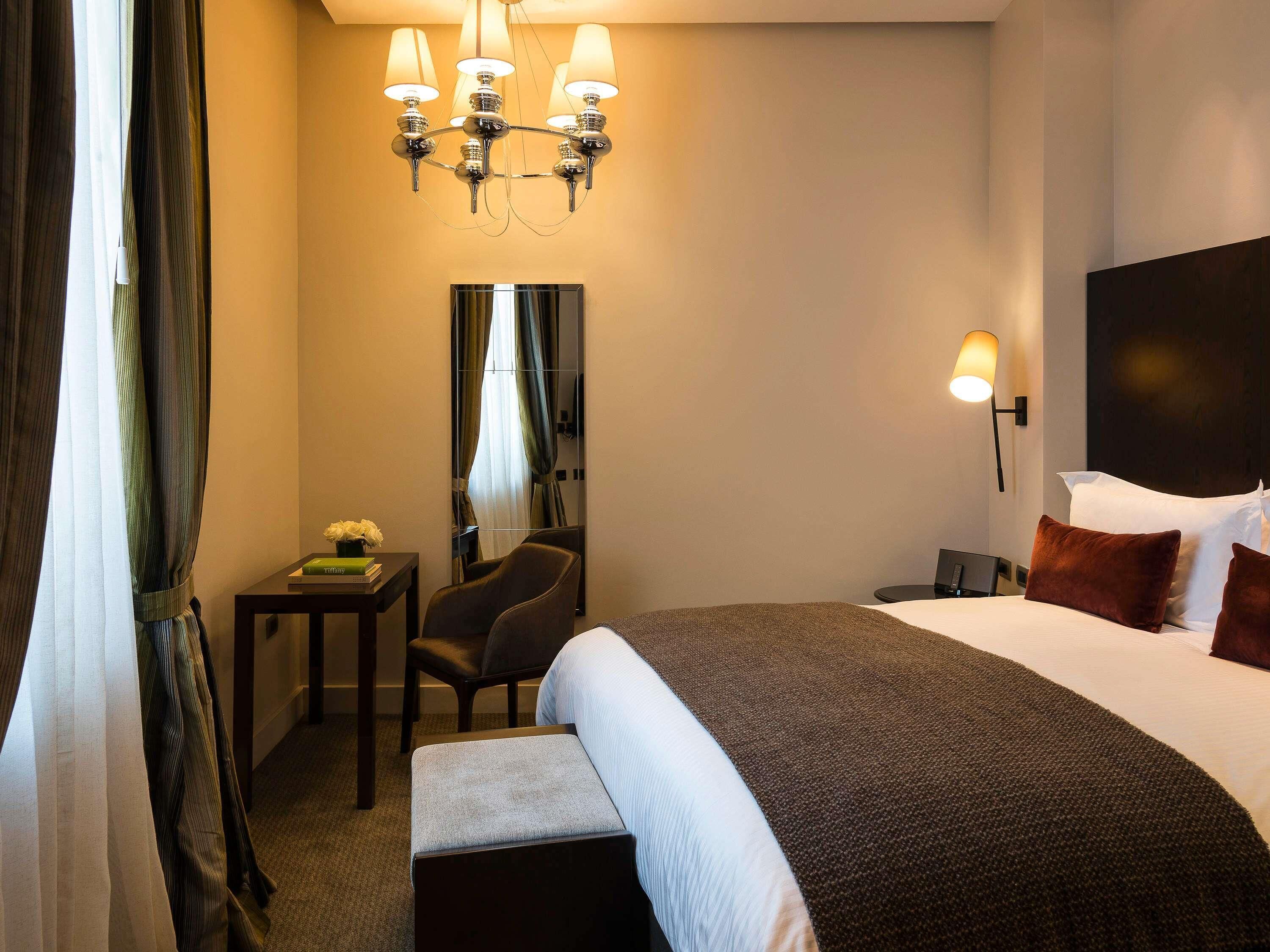 Une chambre d’hôtel avec un grand lit, un bureau avec une chaise, un miroir et un lustre.