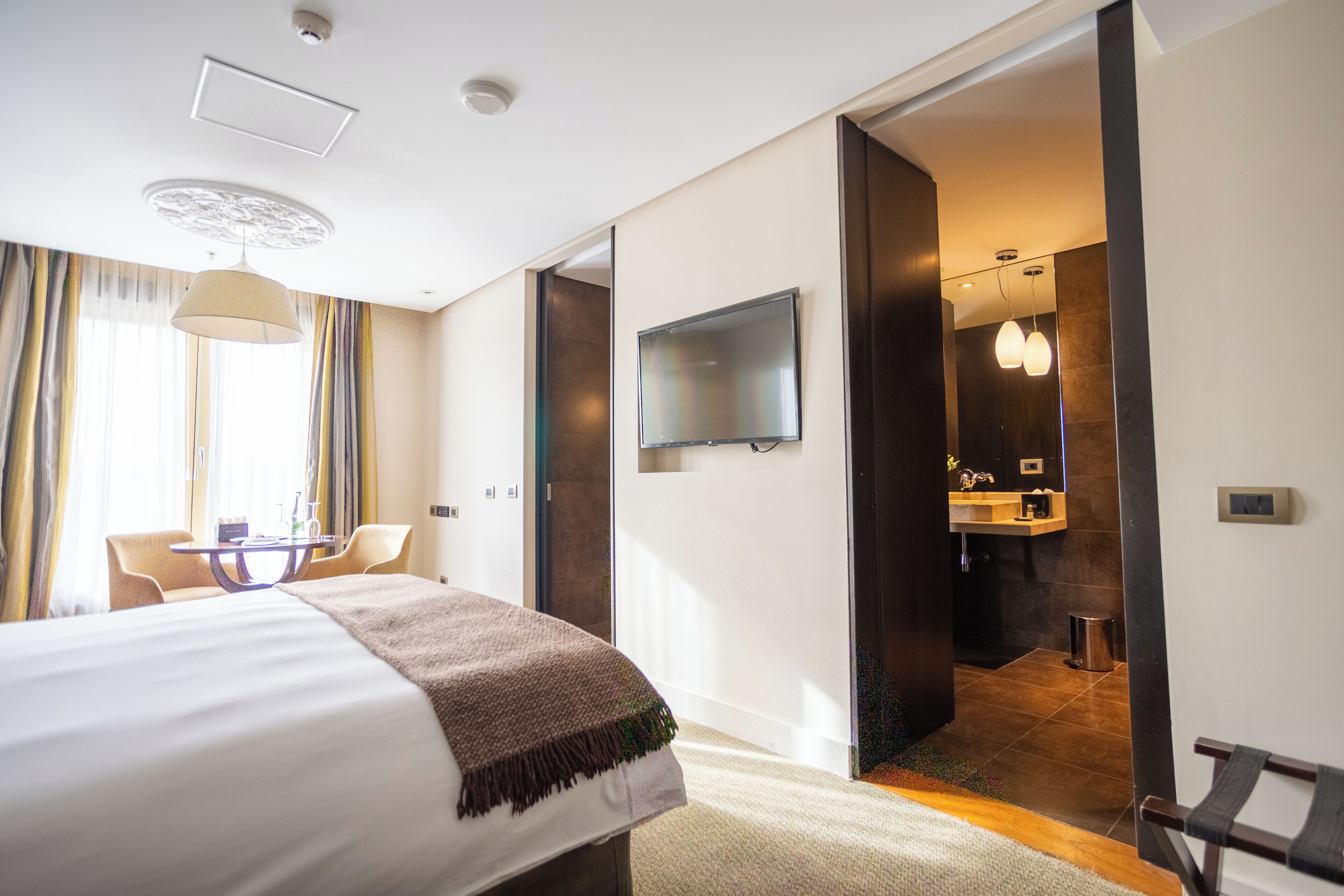 Habitación de hotel con cama, televisor, escritorio y baño visible a través de una puerta abierta.