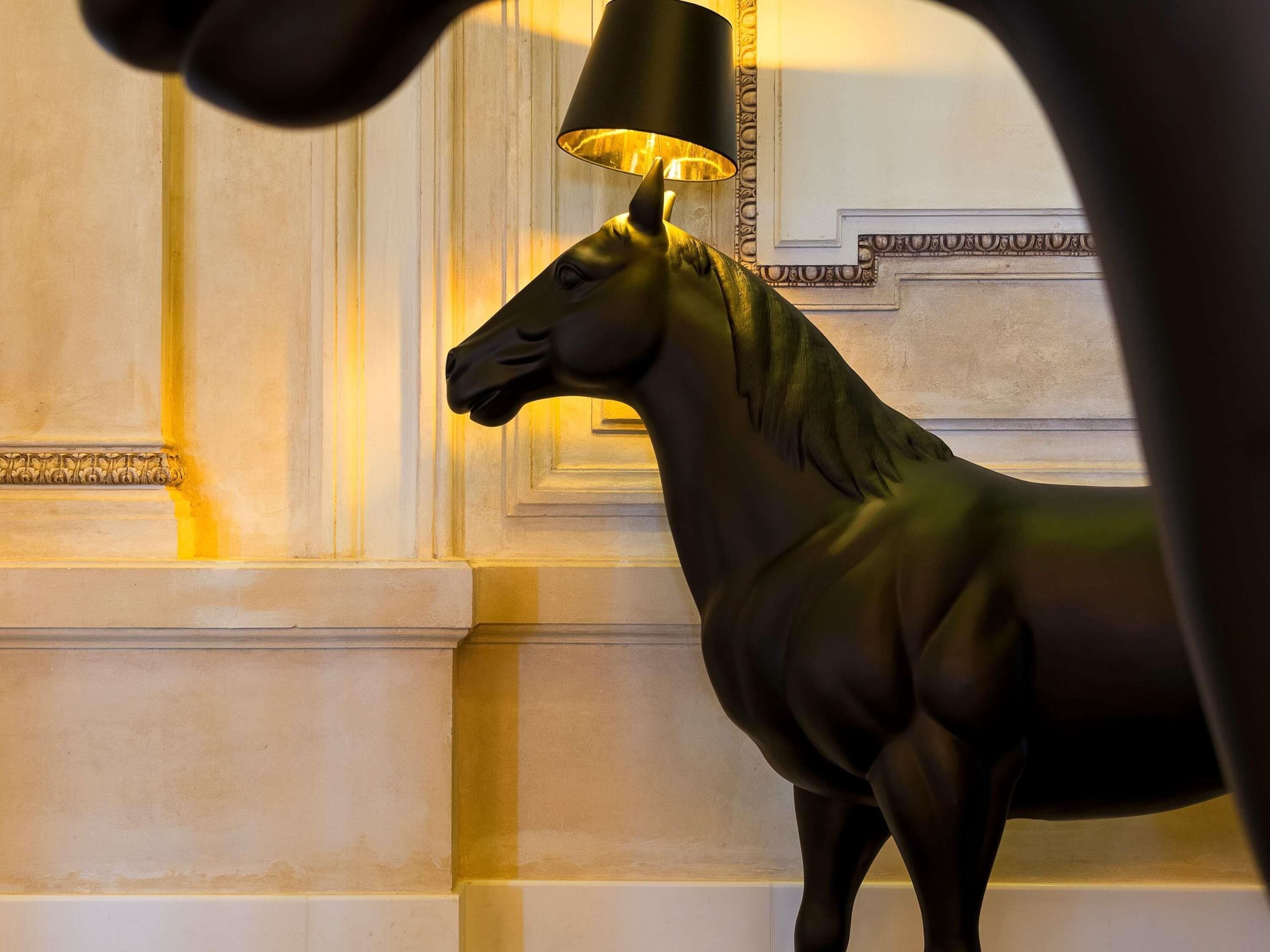 Una estatua de un caballo con una lámpara en la cabeza, frente a un muro con molduras decorativas.