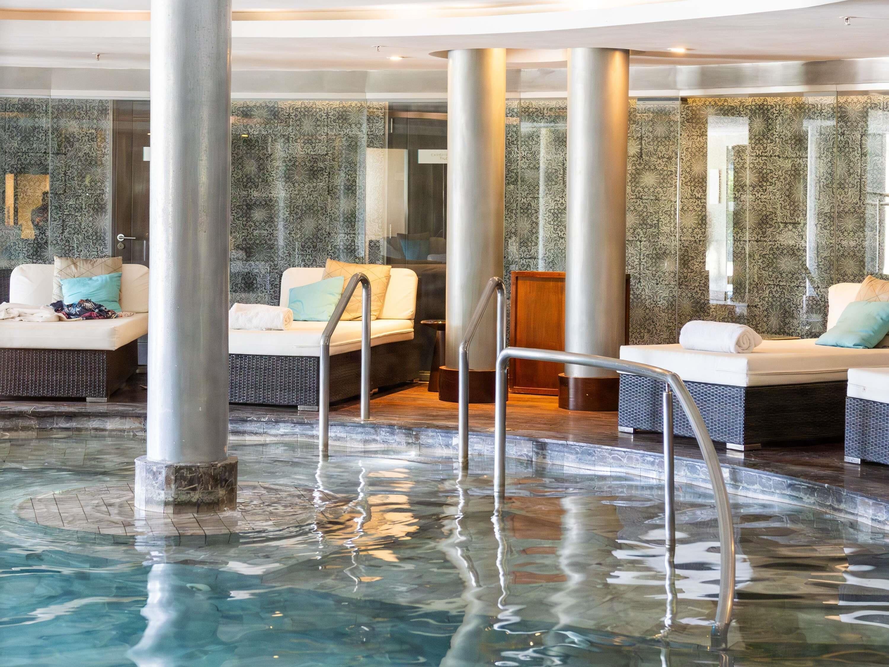 Zona de spa con hidromasaje, asientos y una sala acristalada con paredes decoradas.