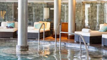 Zona de spa con hidromasaje, asientos y una sala acristalada con paredes decoradas.