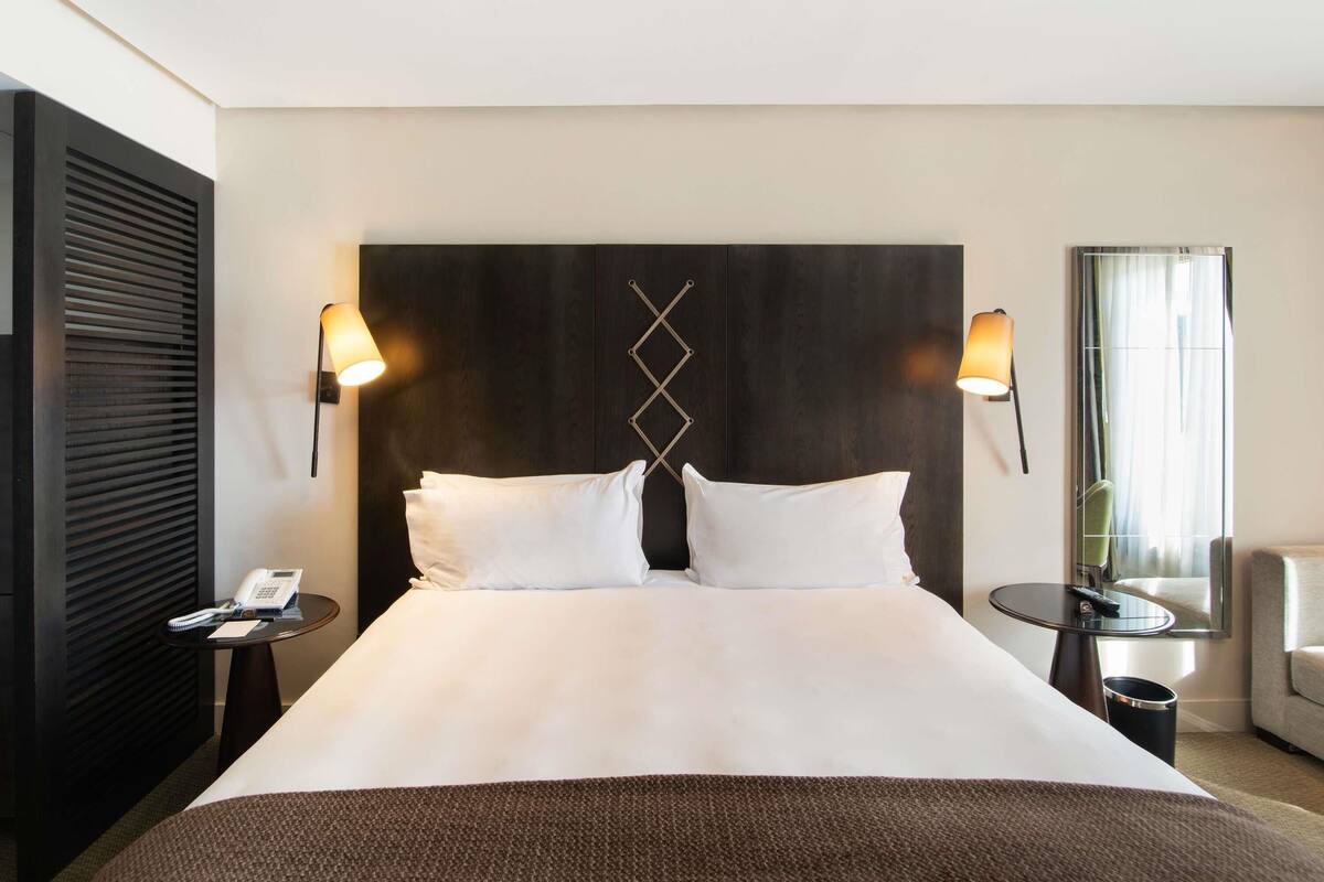 Une chambre d’hôtel avec un grand lit, deux lampes de chevet, un téléphone et une petite table.