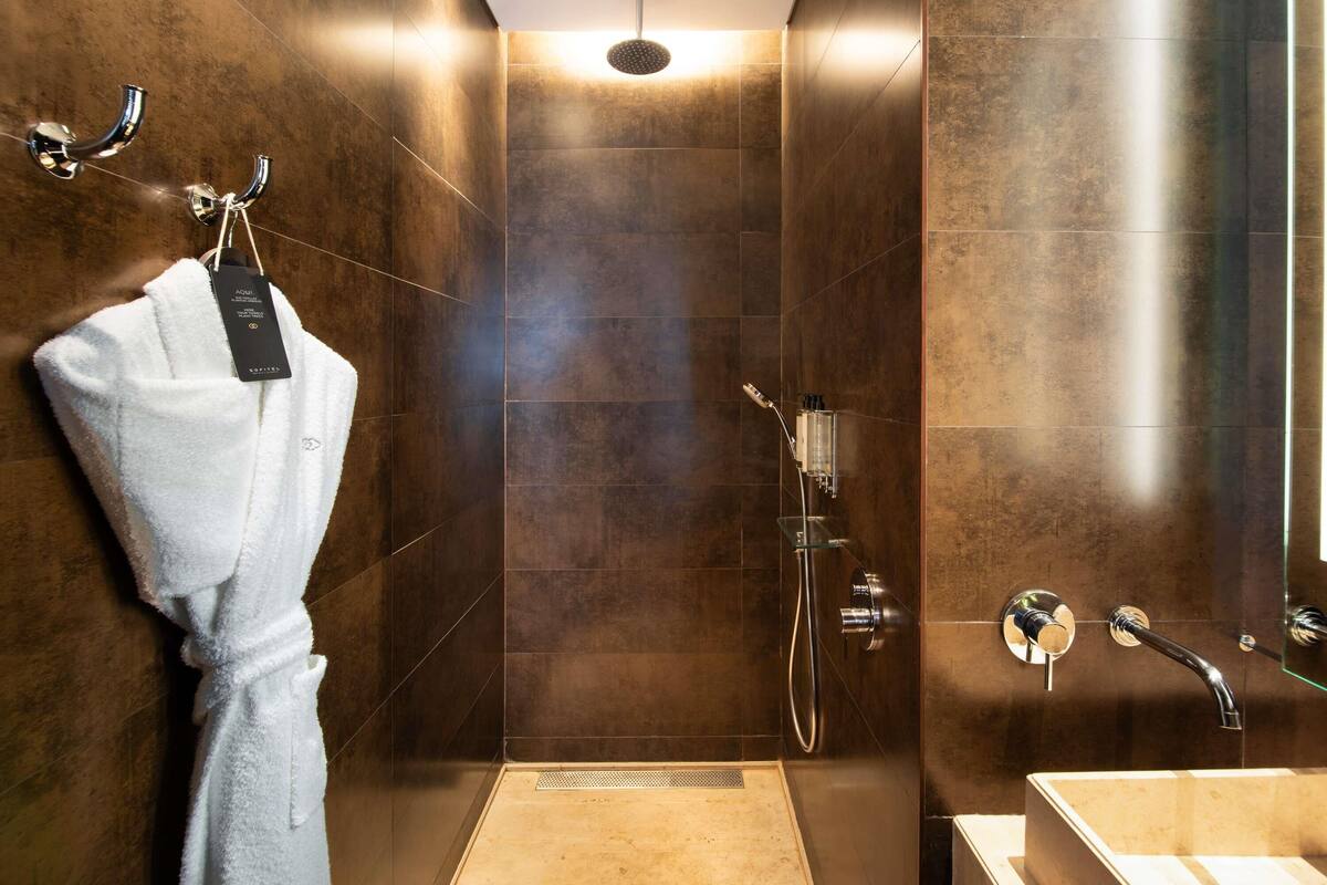 Une salle de bain moderne avec une douche à l’italienne, un lavabo entouré de verre et un porte-serviettes avec un peignoir.