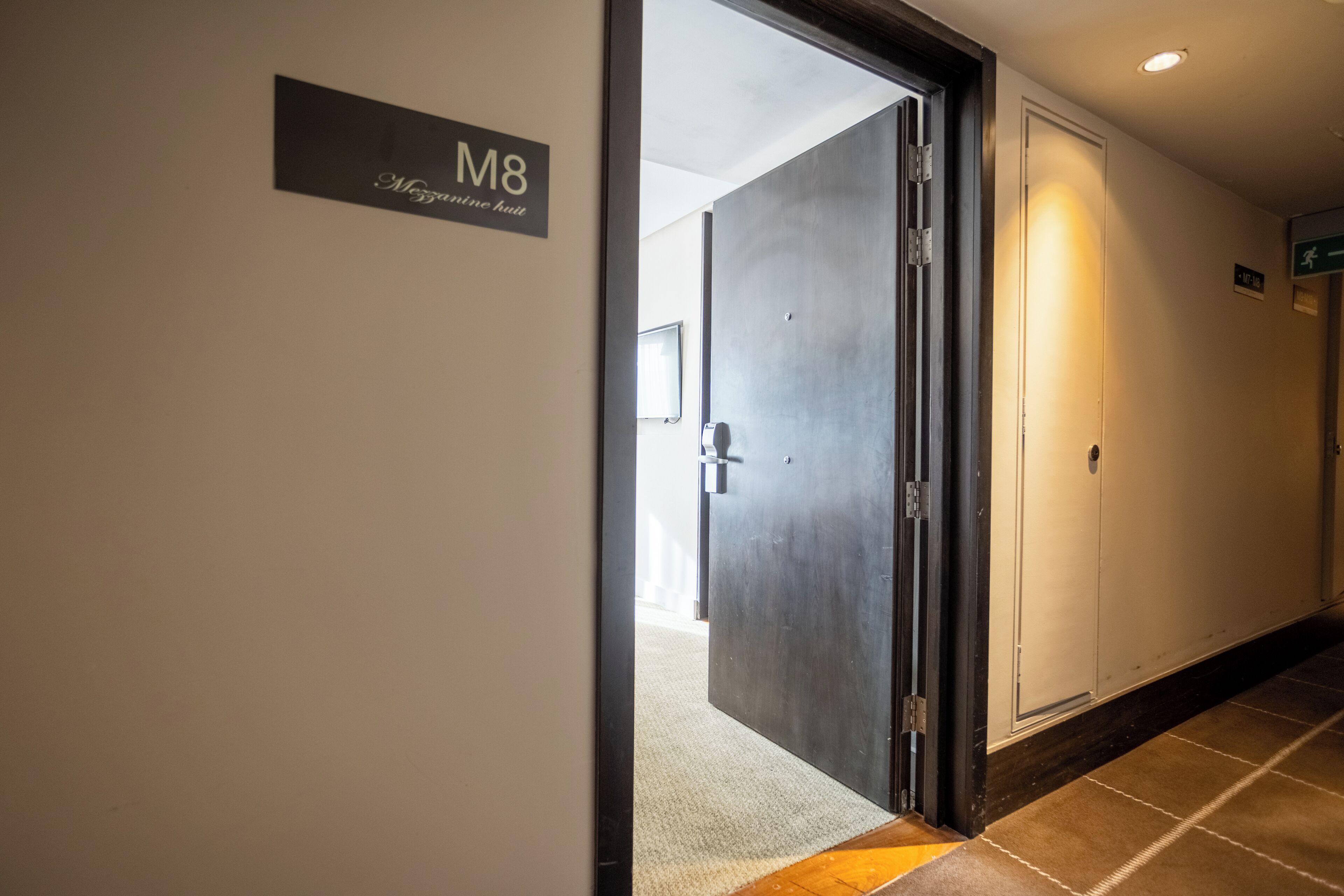 Un pasillo de hotel con un letrero que dice 'M8' y una puerta que da a otra habitación.