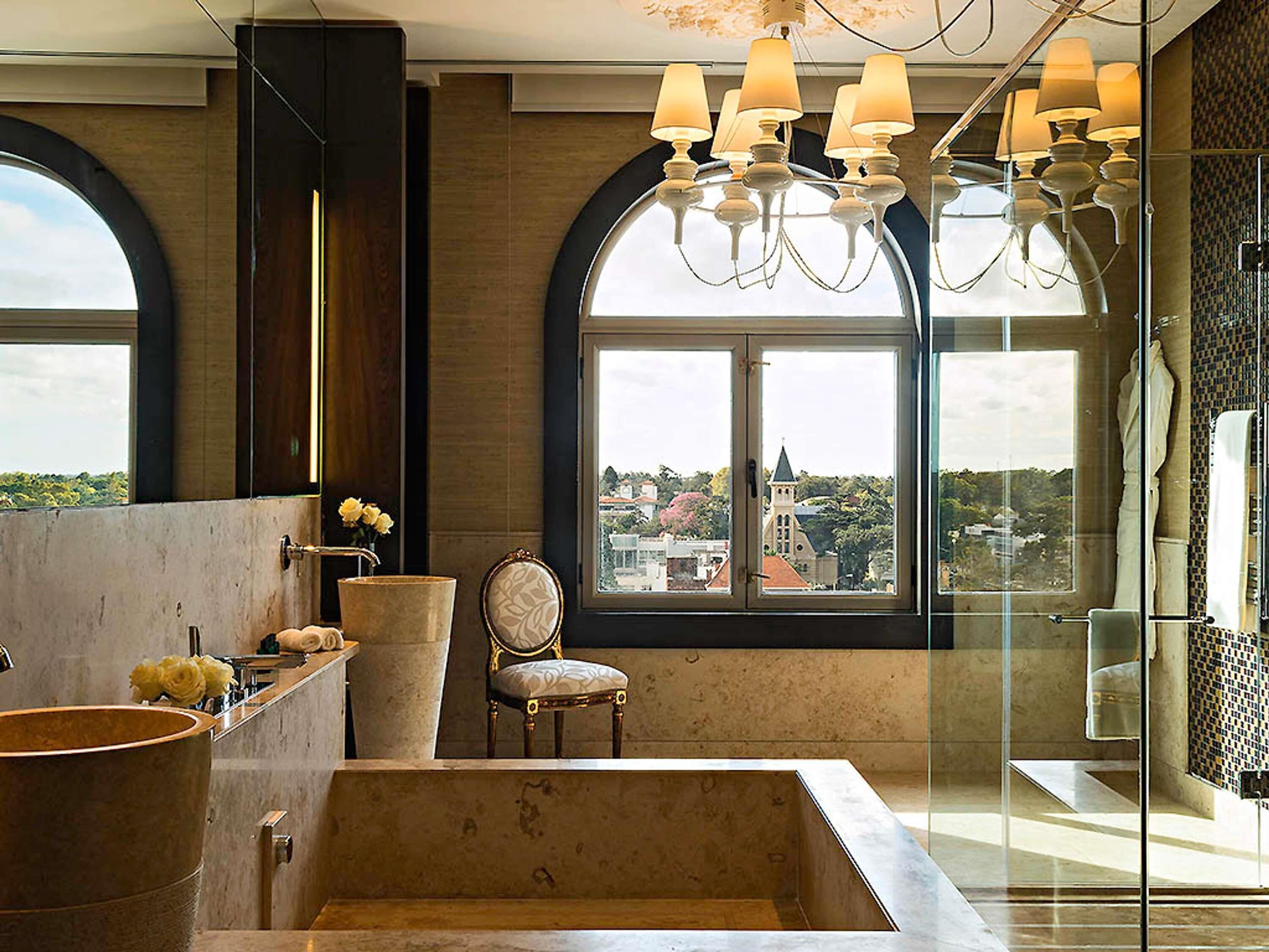 Une salle de bain moderne avec une baignoire, un fauteuil et une grande fenêtre donnant sur des immeubles.