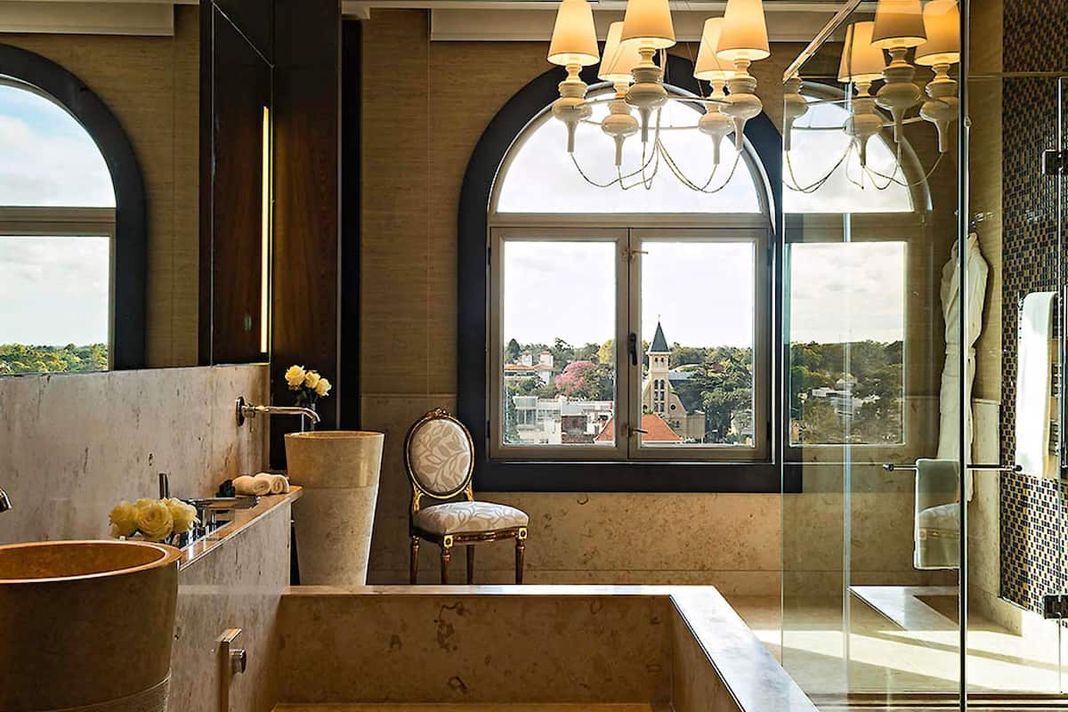 A modern bathroom with a bathtub, a chair, and a large window with a view of buildings.