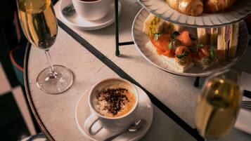 A table with a glass of champagne, a cup of tea, a plate of croissants, and a plate of sandwiches.