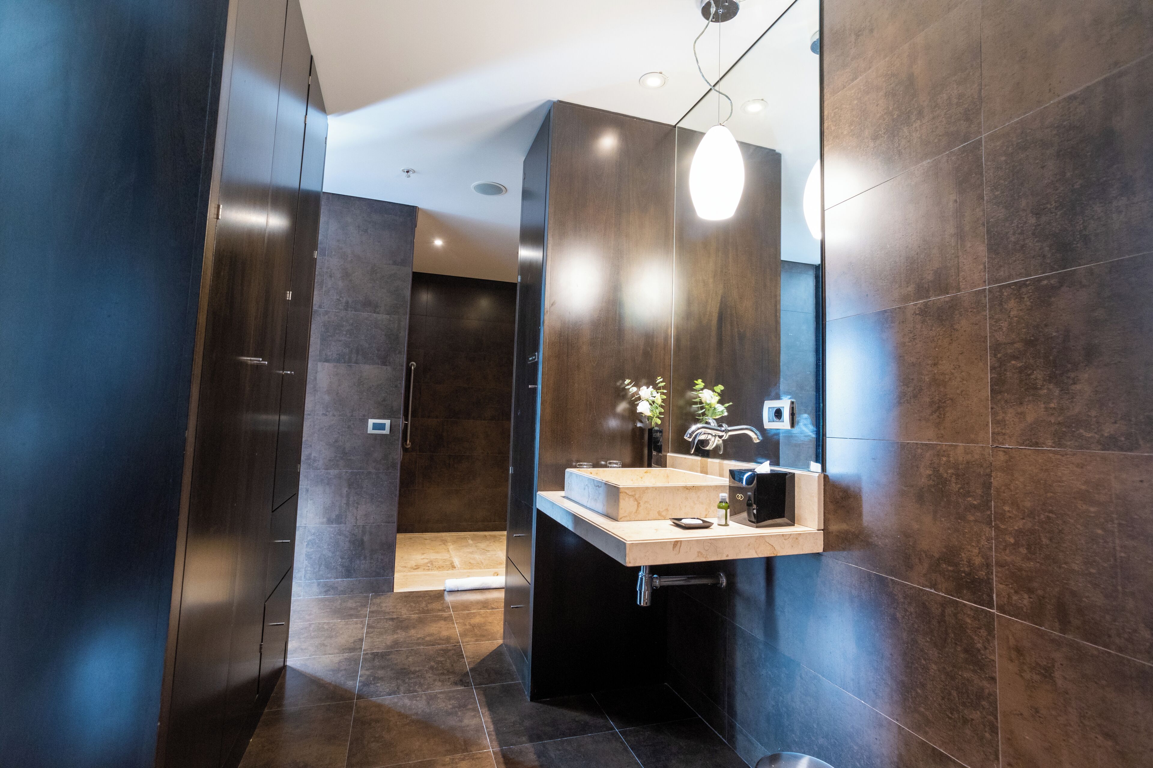 A modern bathroom with dark tiles, a wooden vanity, and a shower area.