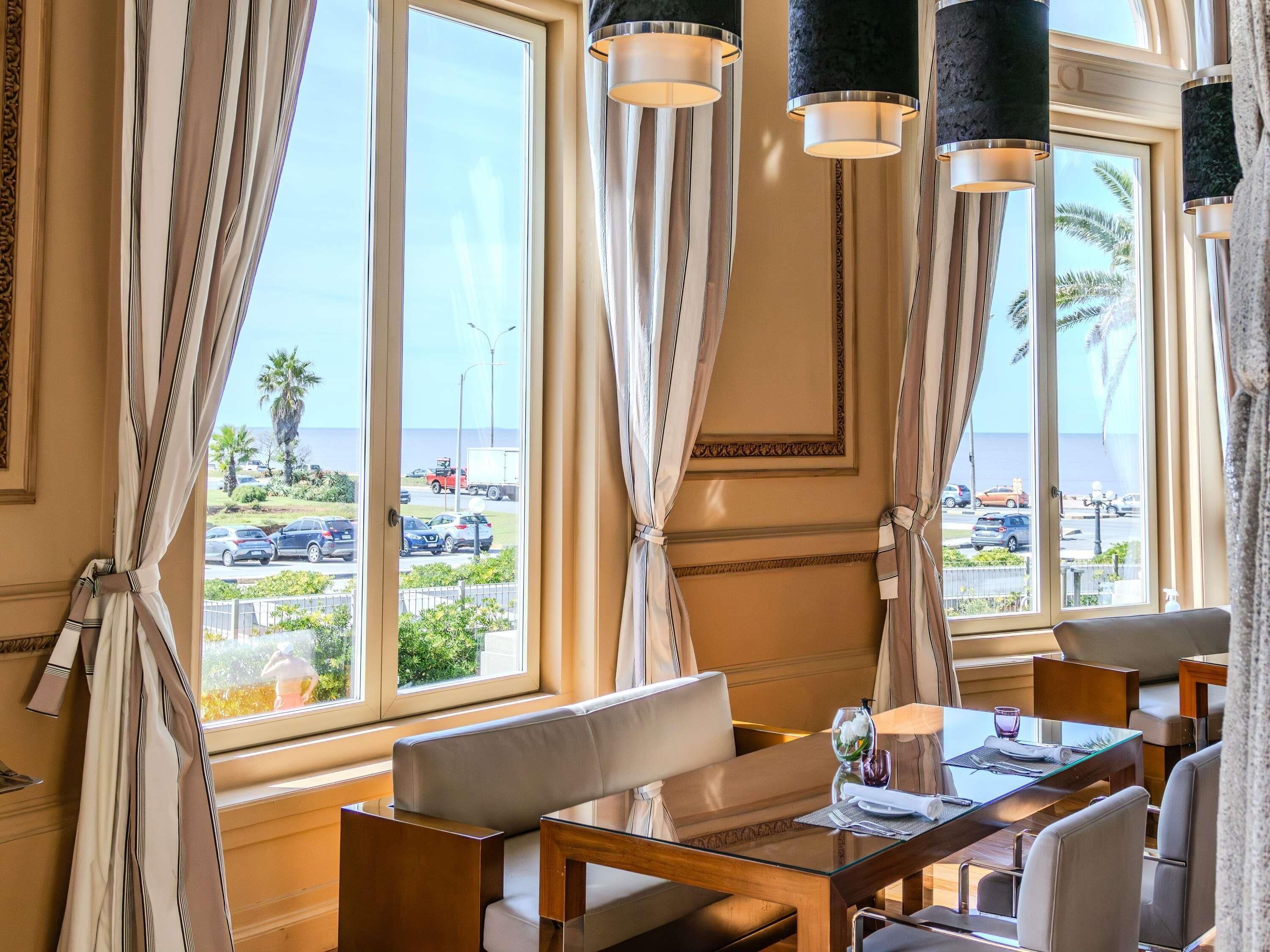 Una habitación de hotel con un ventanal grande, un sofá, una mesa de comedor y una araña.