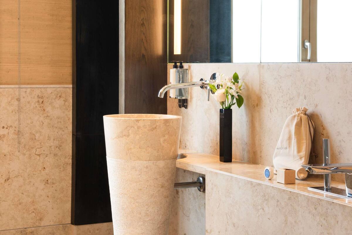 Une salle de bain avec un grand lavabo en marbre, un miroir, un porte-serviettes et une petite poubelle.