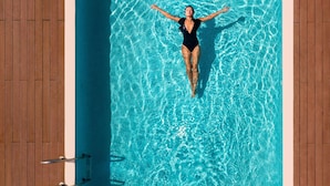 Une personne flotte dans une piscine, qui est entourée d’une terrasse en bois.