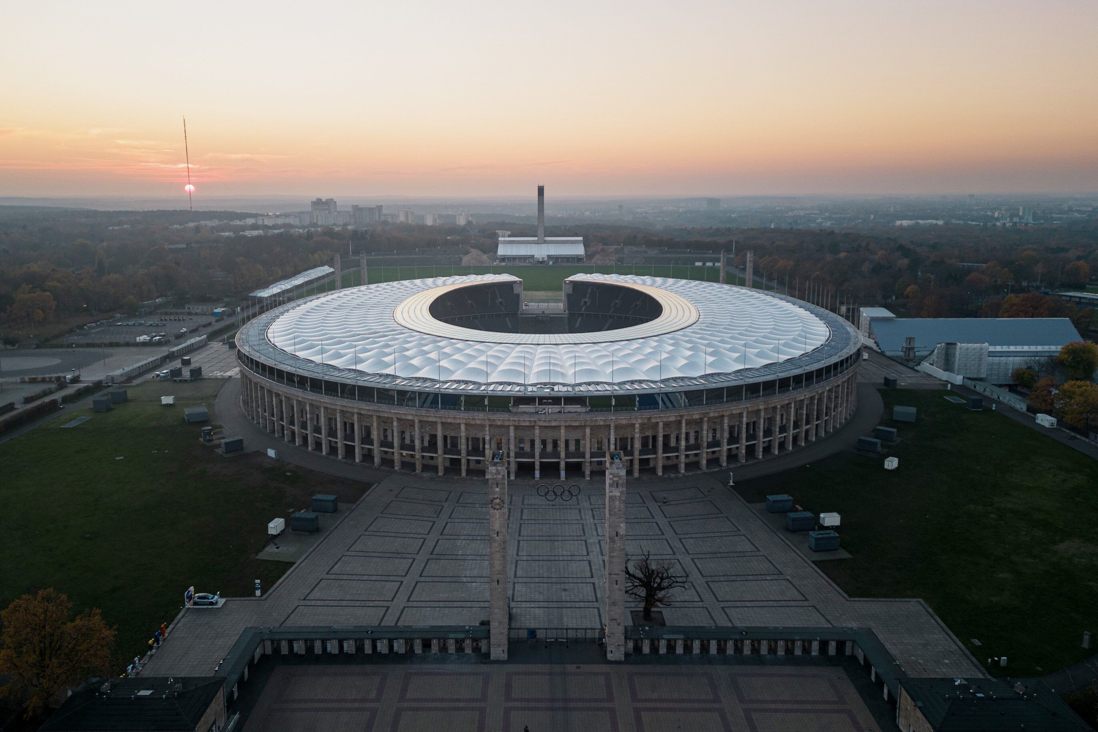 A circular building with a central open area, surrounded by a paved plaza and a few trees.