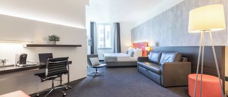 Una habitación de hotel moderna con escritorio, silla de oficina, sofá y reposapiés.