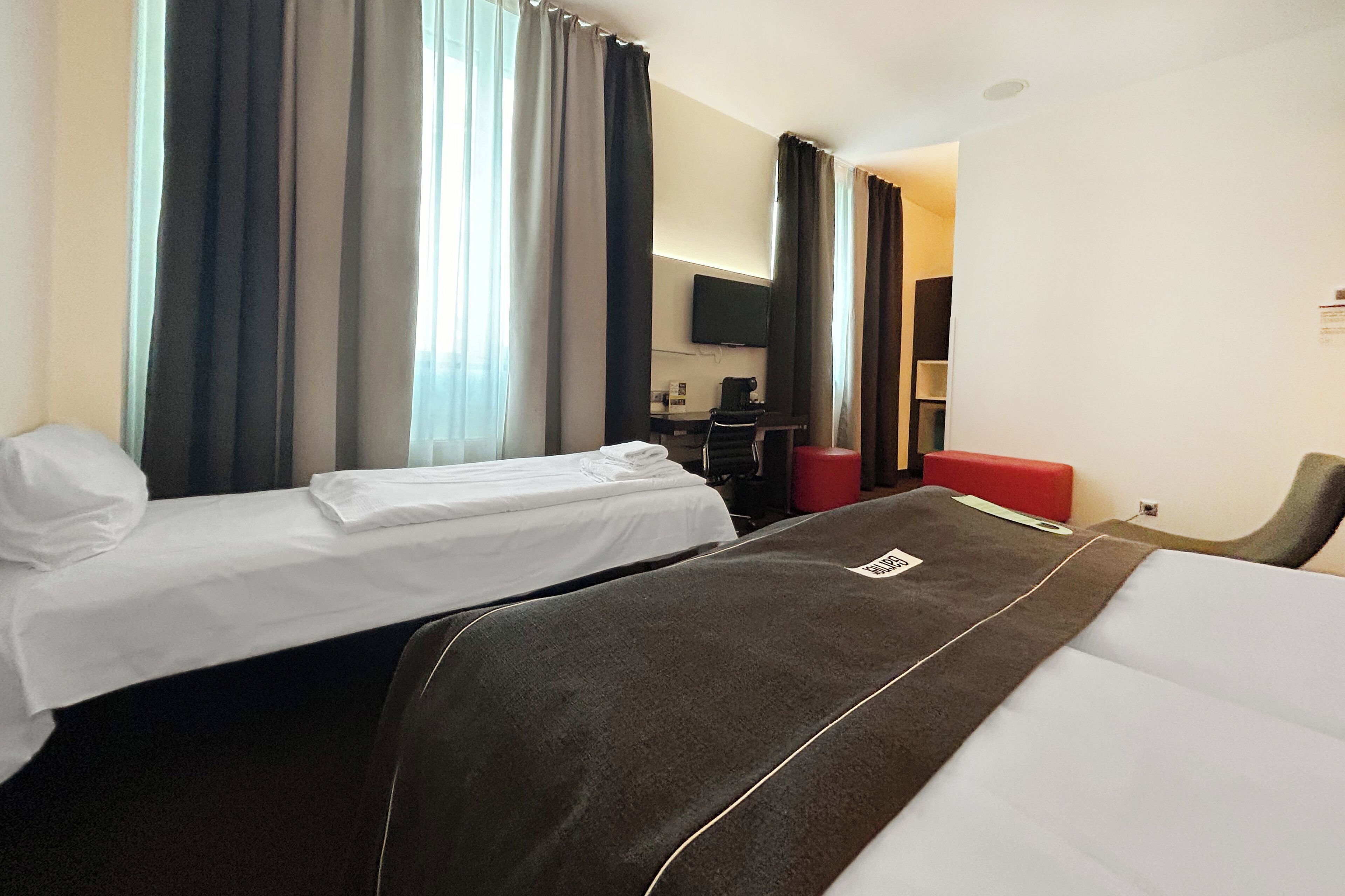 A hotel room with two beds, a desk, a chair, and a TV.
