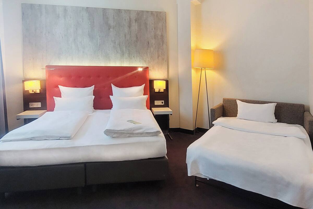 Une chambre d’hôtel avec deux lits, chacun doté de draps et d’oreillers blancs, d’une tête de lit rouge et de lampes de chevet.