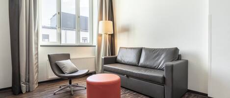 A modern living room with a grey sofa, a red ottoman, a grey armchair, and a floor lamp.