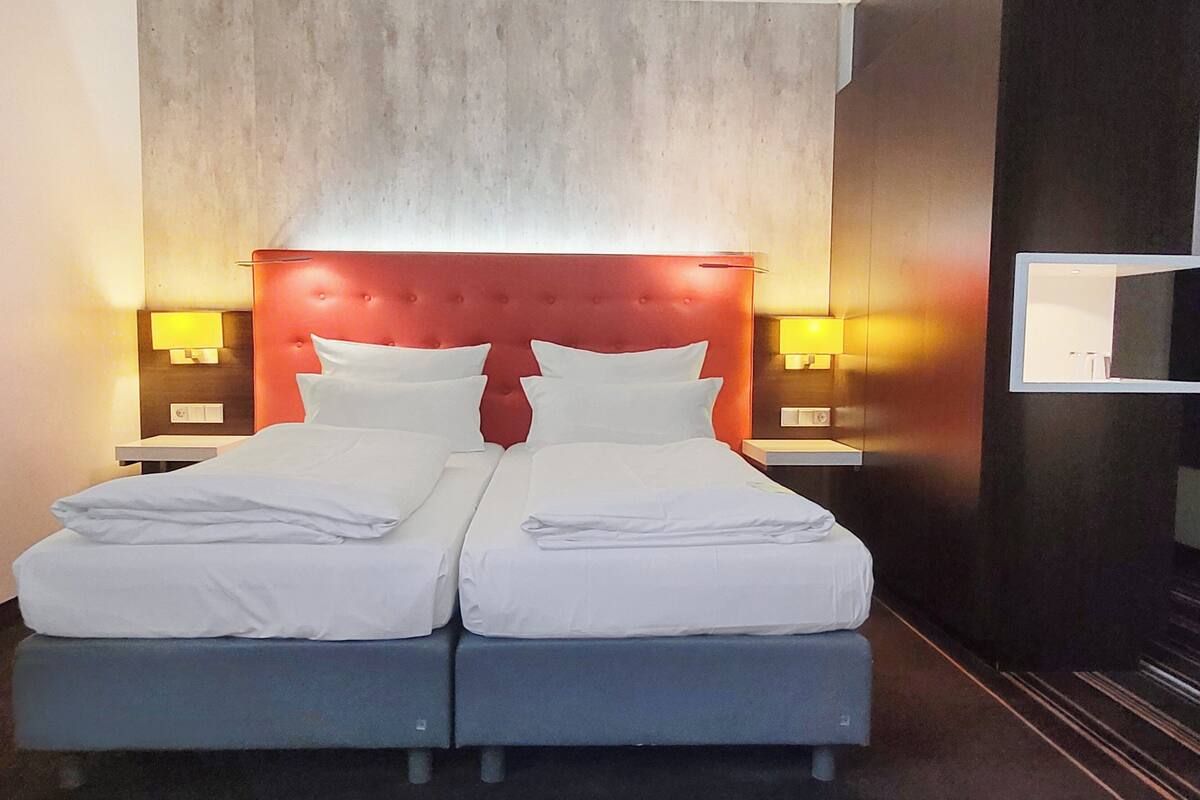 Un lit double avec une tête de lit rouge, deux tables de chevet avec des lampes et un miroir au mur.