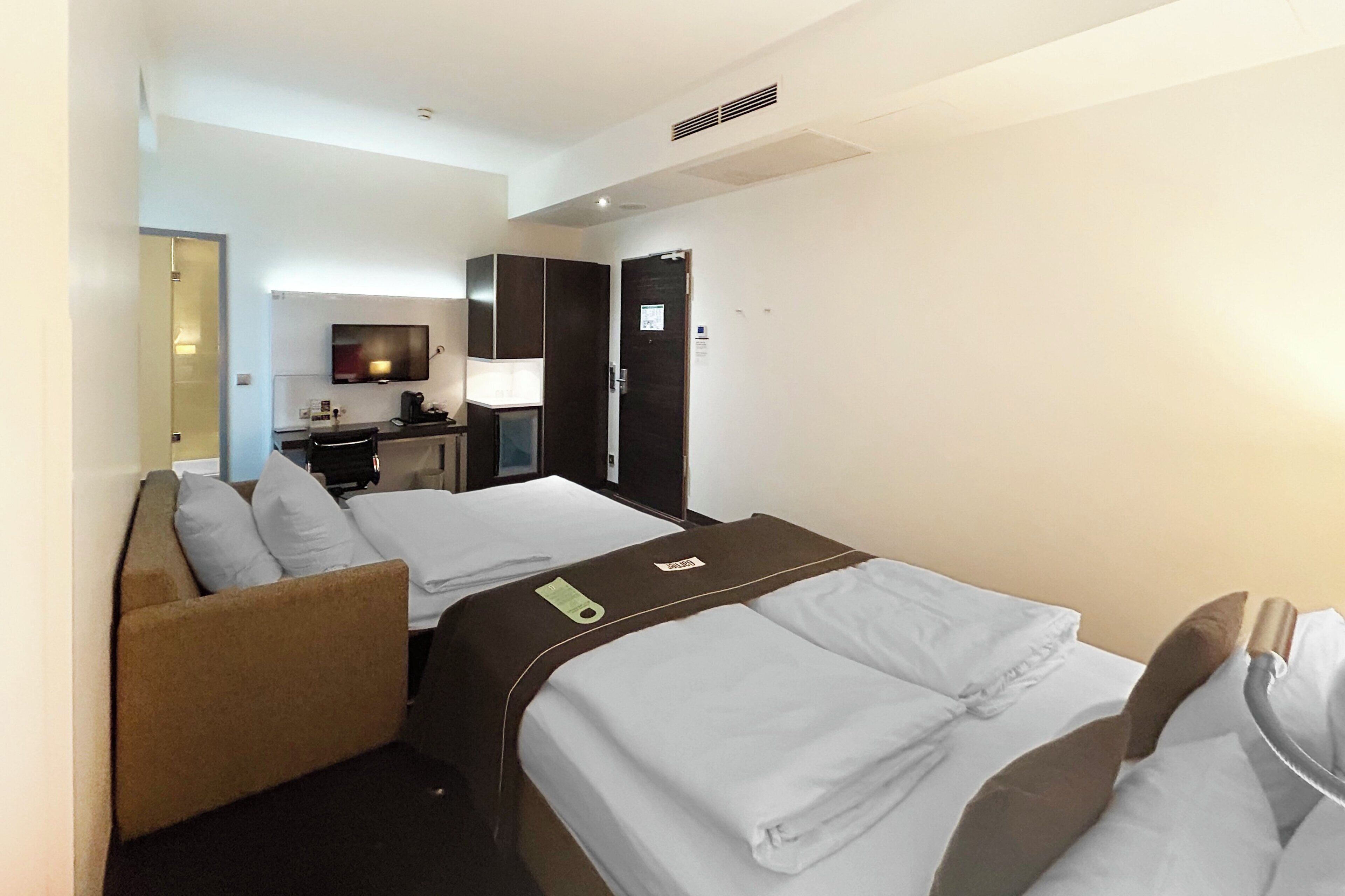 Habitación de hotel con dos camas, un sofá, un escritorio, un televisor y la puerta del baño.
